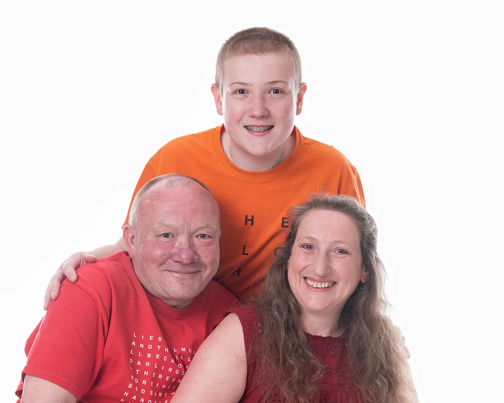 A boy in a orange t-shirt towers behind his parents in front in a very white room