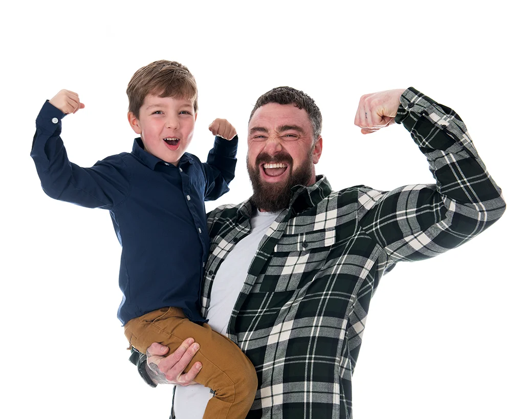 Strong looking father lifting his seven year old son with one arm while both are showing their arm muscles while cheering while bright white background