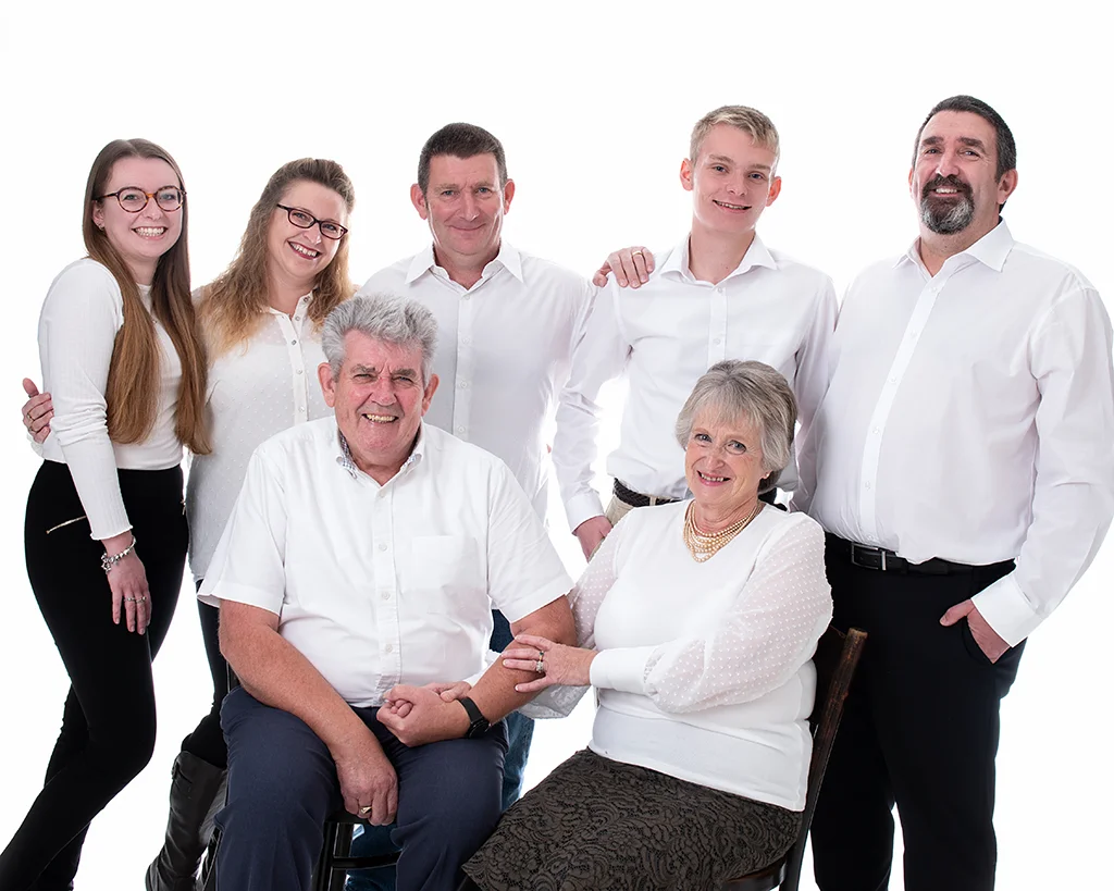 Nan and grandad sitting in front of their two sons, one daughter in law and two grand children all wearing white tops in a very white room