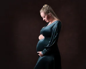 A pregnant woman in a velvet dress posing on a dark background.
