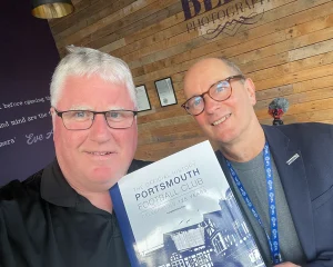 Two men holding up a book in front of a wall.