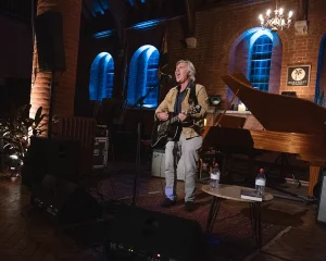 Former Sex Pistol Glen Matlock standing on stage with a guitar.