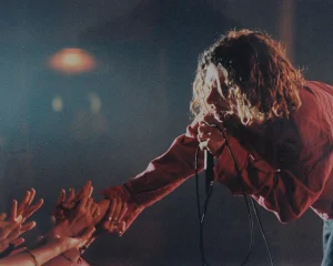 INXS's Michael Hutchence red shirt is singing into a microphone.