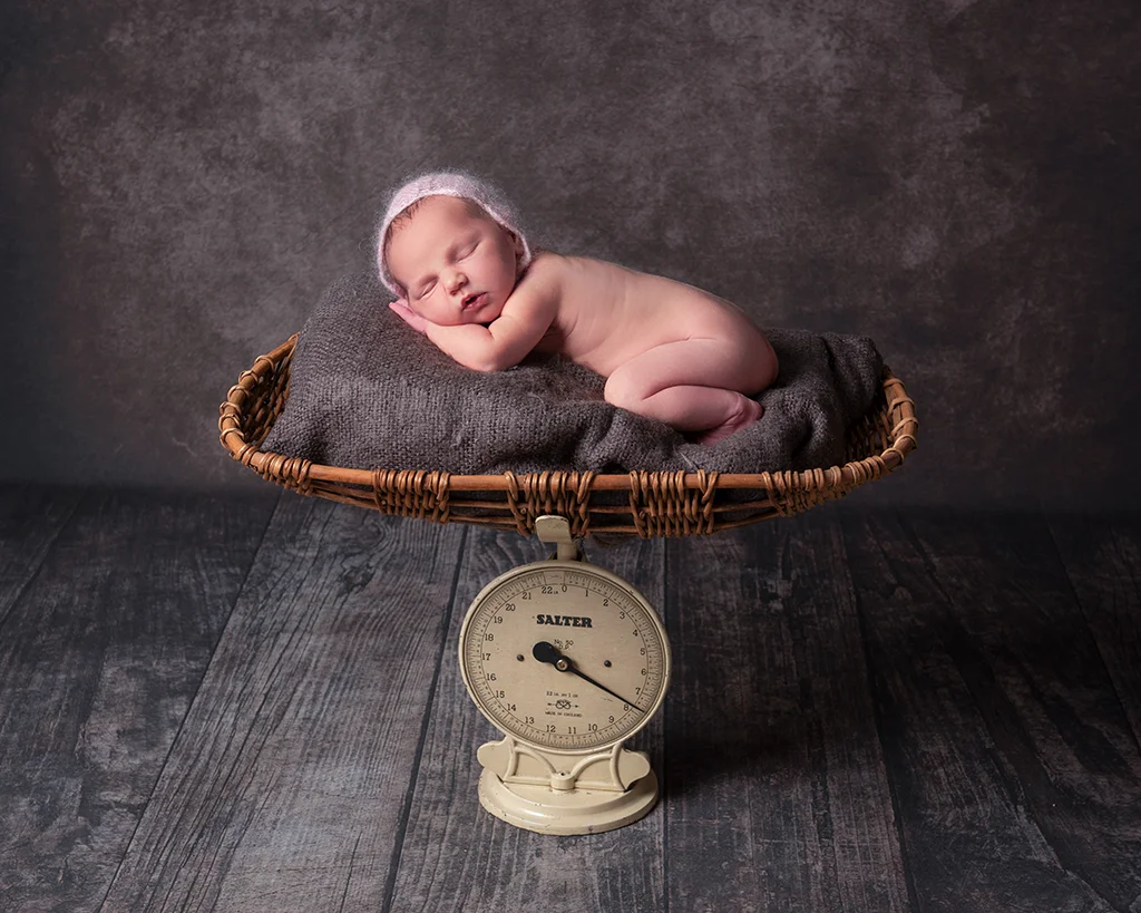A newborn baby is laying on a scale in a wicker basket.