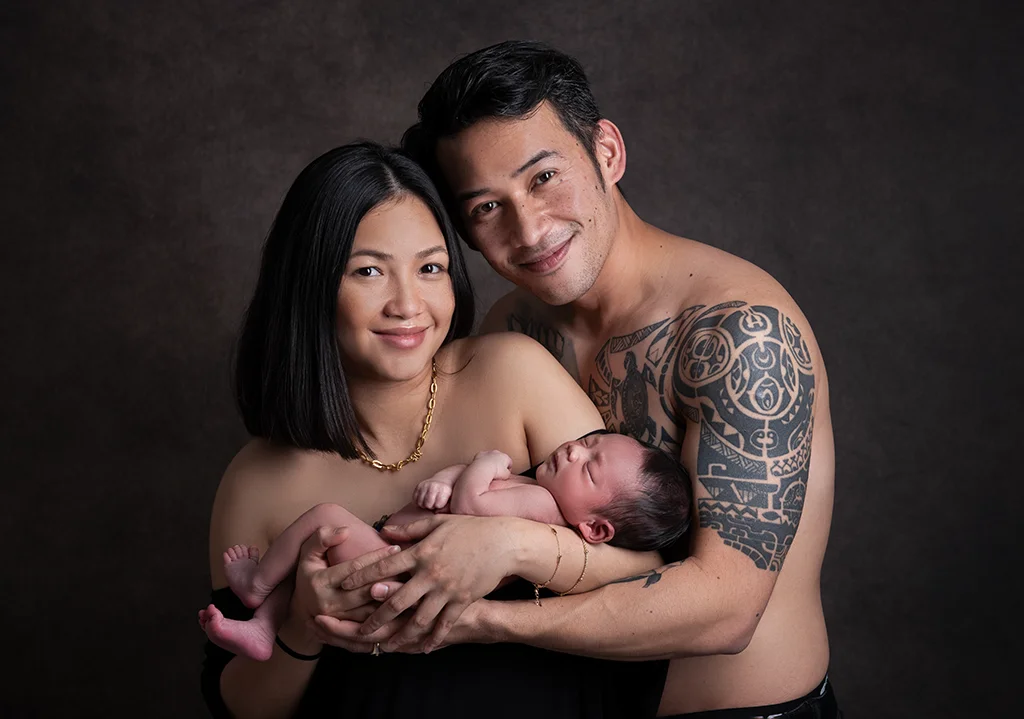 A man and woman with tattoos posing with their newborn baby.